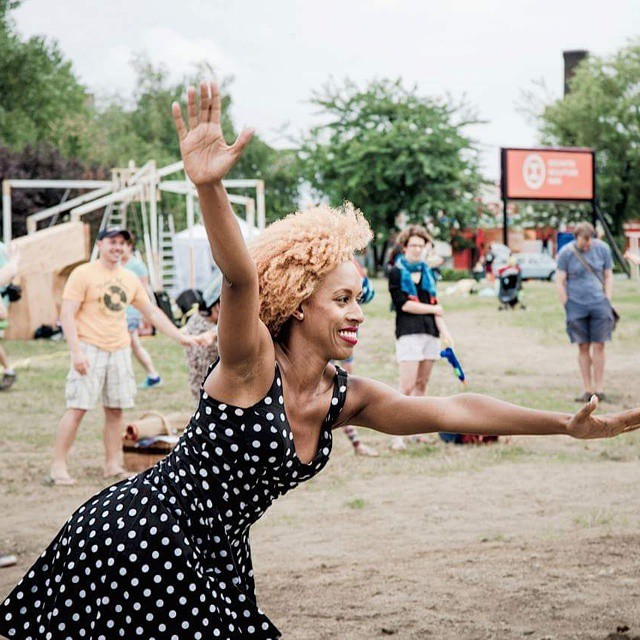 A woman in a black and white polka-dot dress with her arms extended and a big grin on her face